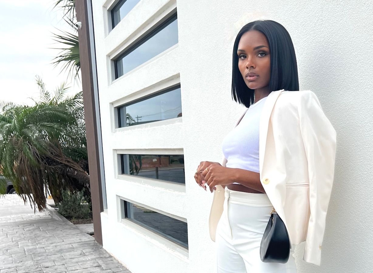 London posing against modern white architecture in an ivory suit